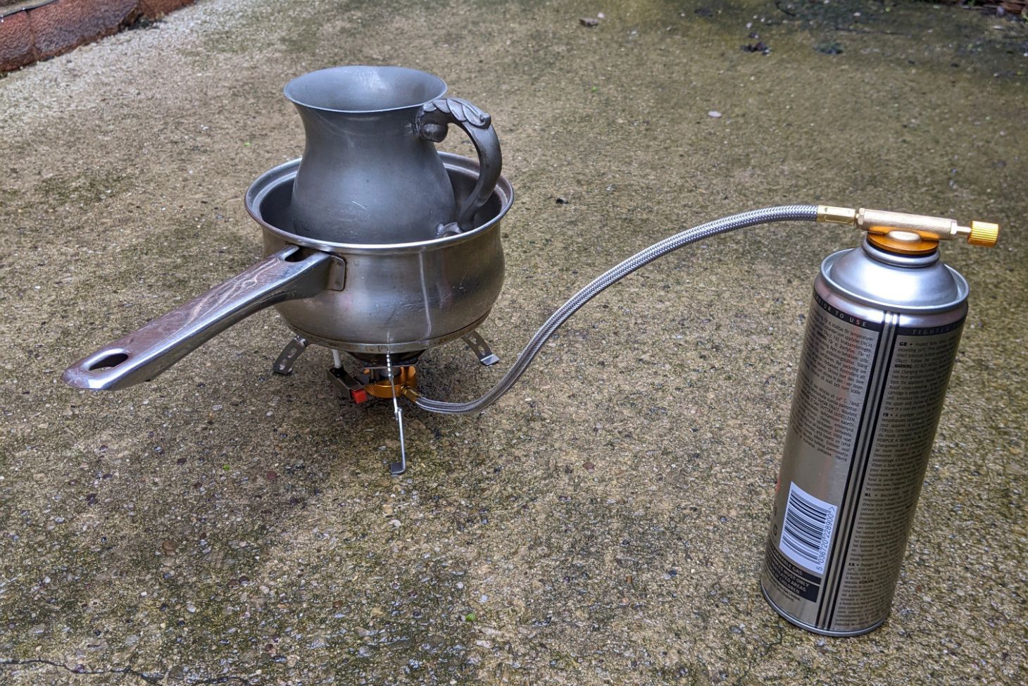 Pewter tankard ready to be melted in a saucepan over a gas camping stove.